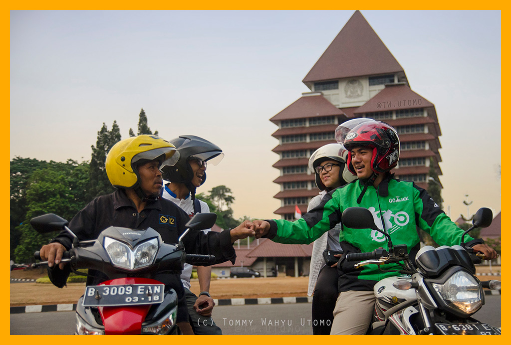 Gojek driver fist-bumps with ojek driver in front of Universitas Indonesia