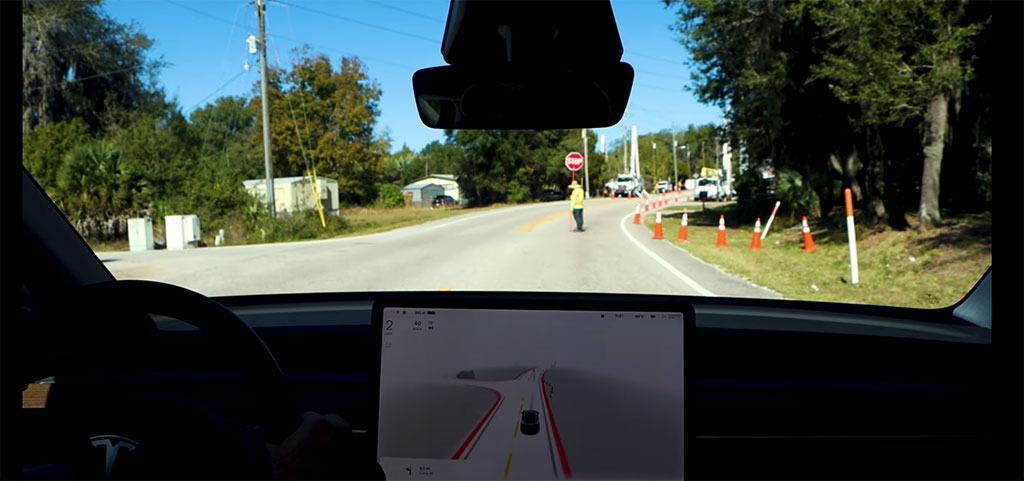 View through a car's windshield shows a person holding a stop sign, standing in the middle of a road